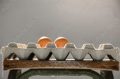 Two eggs are placed in a carton on the ancient chair. The white wall is the background 