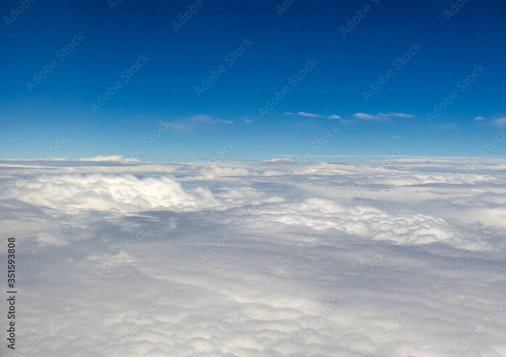 Gorgeous dense clouds and the bright blue horizon of the sky from the height of a flying airplane. Smooth calm landscape of white clouds. Sky background with space for text.