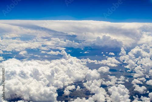Magnificent fluffy clouds and the bright blue horizon of the sky from the height of a flying plane. A beautiful sky background of white clouds that cast a shadow on the ground. © Ninaveter