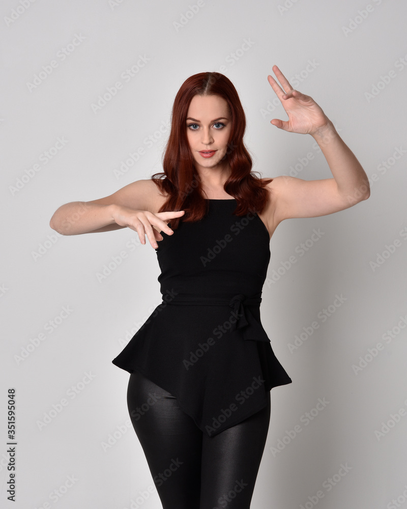 3/4 portrait of a pretty girl with red hair wearing black leather pants and top. isolated against a studio background 3/4 portrait of a pretty girl with red hair wearing black leather pants and top. isolated against a studio background
