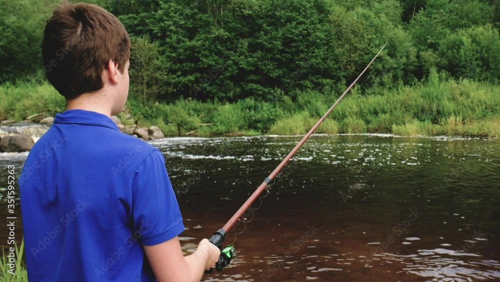 teenager boy stands on the riverbank with a long fishing rod. fishing. side view. close-up. water threshold, waterfall. summer. teenager boy stands on the riverbank with a long fishing rod. fishing. side view. close-up. water threshold, waterfall. summer.