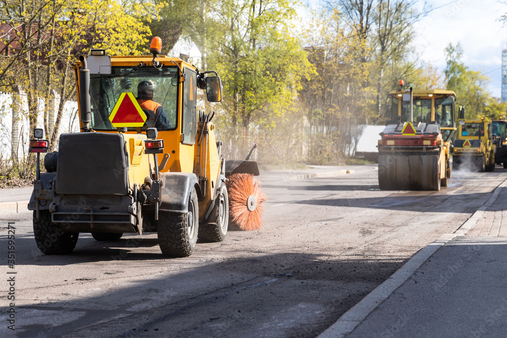 Tractor with spinning brush cleaning newly laid asphalt. Reconstruction and repair of a street road, municipal work. Tractor with spinning brush cleaning newly laid asphalt. Reconstruction and repair of a street road, municipal work.