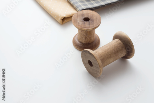 Vintage french wooden empty sewing reels and cuts of fabric on a white wooden surface against a white curtains background.