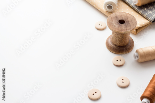 Retro sewing items: sewing thimbles, wooden buttons, vintage wooden reels with multi-colored thread, natural fabric on a white background.