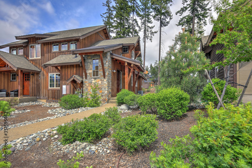 Classic rustic new home in dark brown wood exterior with forest landscape with front natural landscaping.