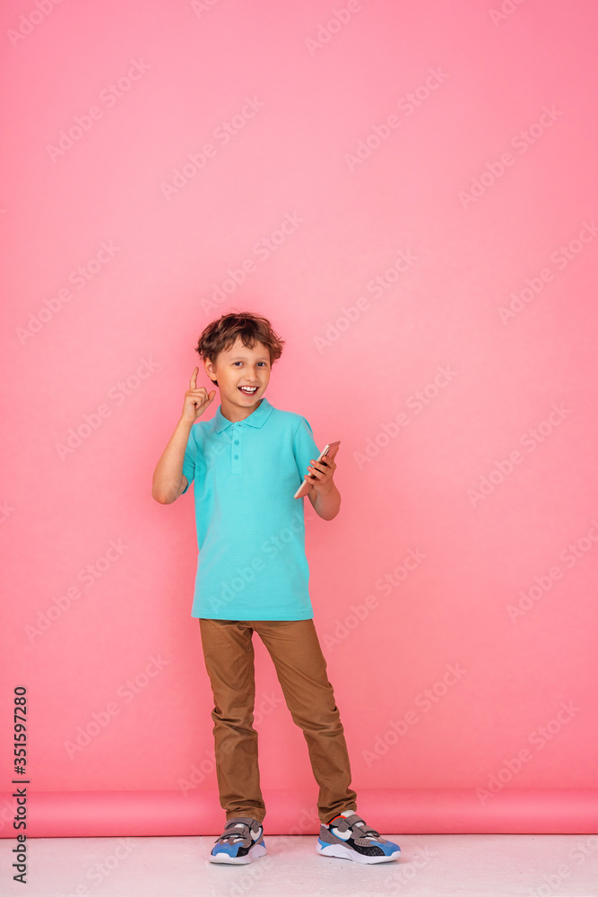 boy, holds a smartphone in his hands and points up against a pink background.