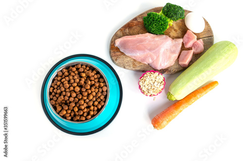 Foreground bowl with dry food for animals and various ingredients of healthy food in the background. Dog food concept. Top view