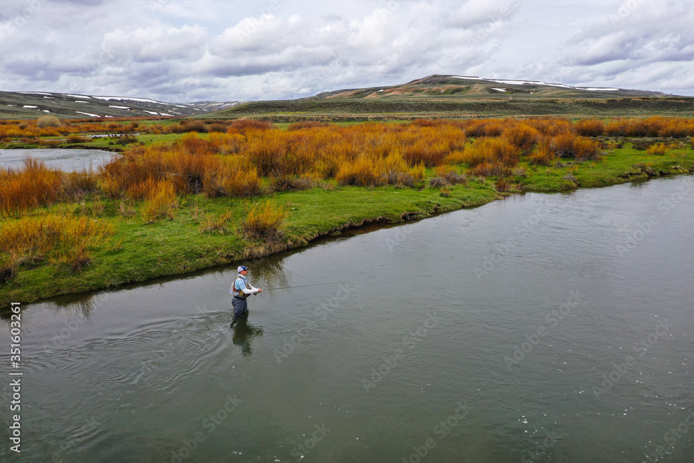 an aerial shot of a man fly fishing on a river.