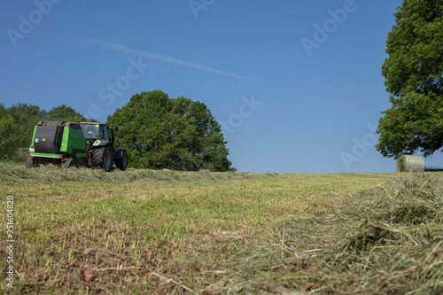 Heuernte  im Frühjahr mit Traktor und Ballenpresse,
der erste Grasschnitt wird zu Rundballen gepresst. photo