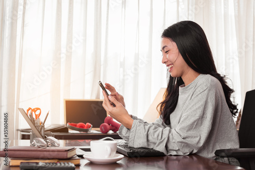 Young Asian woman is working at home. Freelancer is using phone for work. work at home concept. © C_Production