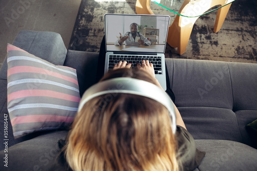 Young woman getting online medical help and advice during videocall with doctor checking symtoms aand explaining the drug's reciepes. Connection during self-insulation using laptop, headphones, phone. photo