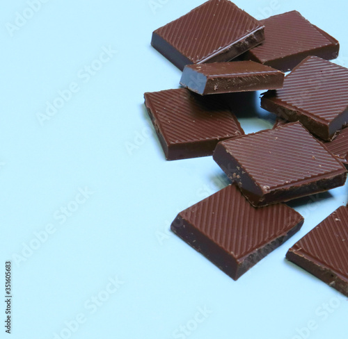 a bar of dark chocolate is broken into pieces, lies on a blue background. Place for text, inscriptions. Sweet life, international chocolate festival, sugar addiction, consumption