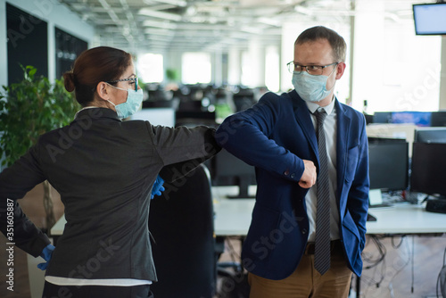 Office workers shake hands when meeting and greet bumping elbows. A new way to greet the obstructing spread of coronavirus. Man and woman in protective masks maintain a social distance at work.