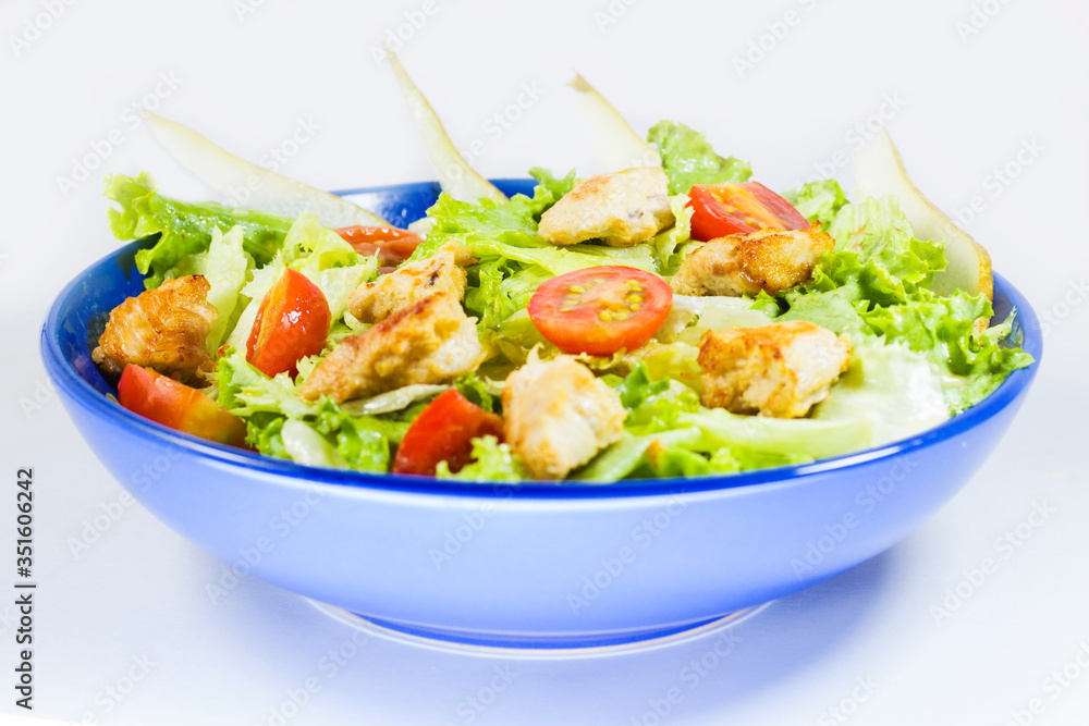 Chicken salad with tomatoes, pear and green salad on the blue bowl, white background. Chicken salad with tomatoes, pear and green salad on the blue bowl, white background.