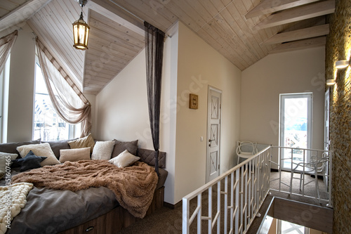 Interior of a modern house spacious hallway with big soft resting place. Contemporary wide sofa with many pillows and light window onder wooden loft ceiling. photo