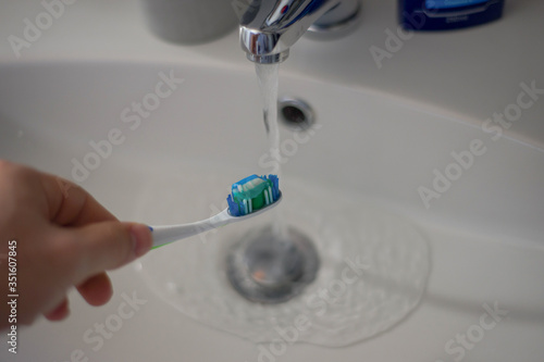 Hand holding toothbrush under running water