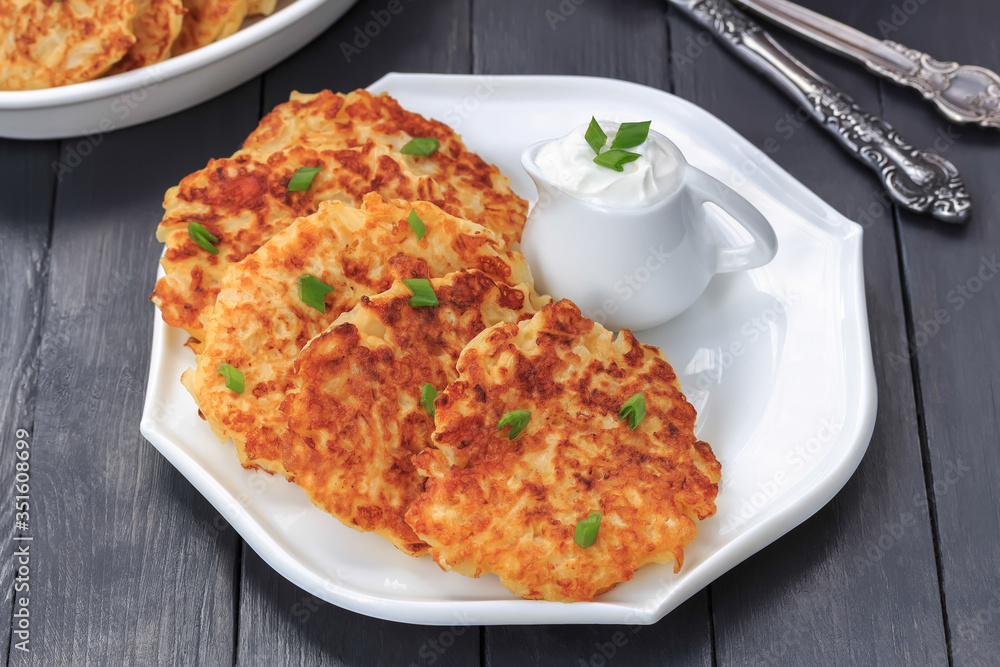 Vegetable fritters. Pancakes with cabbage, green onion and yogurt dressing on white plate. Dark wooden background, close-up