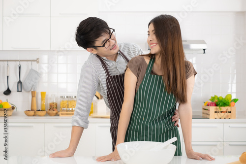 Romantic young Asian couple prepare cooking together in white kitchen.