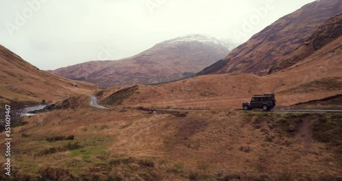 Land Rover Defender driving through amazing Scottish Countryside with huge mountains and large river