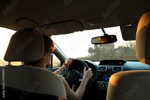 Close up view of a woman driver holding steering wheel driving a car at sunset.
