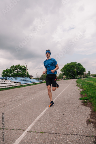 A young athlete in a blue T-shirt runs around the stadium