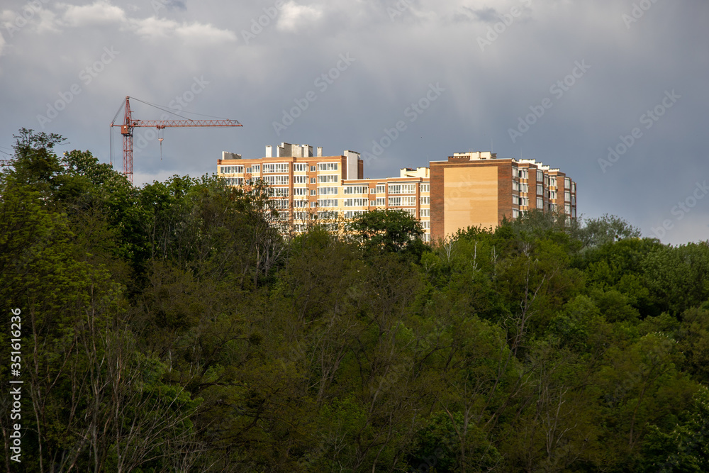 Construction of a high-rise building against the sky of trees and a construction crane