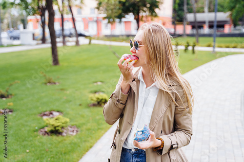 Junk food. Happy delighted woman in casual clothes eating donut with expression of big pleasure, temptation to bite doughnut, appetizing bakery. Sweet tooth,indulgence, gluttony, unhealthy lifestyle © Daria