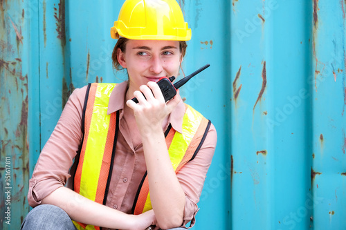 Pretty engineer worker using walkie talkie to control loading containers in the container cargo shipping area. Industrial Container for import and export. Happy work. Shipping and logistic concept