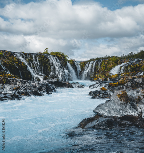 Dramatic views of the bright powerful Bruarfoss bluw waterfall. Popular tourist attraction. Blue sky and clouds during midnight sun. Location place Brekkuskogur South Iceland, Europe.