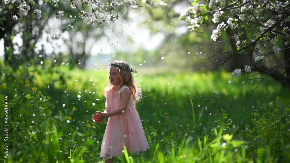 Slow motion Happy little girl in a beautiful pink dress walks in a flowering spring park. It stands near the tree from which the petals are streaming. Slow motion Happy little girl in a beautiful pink dress walks in a flowering spring park. It stands near the tree from which the petals are streaming.