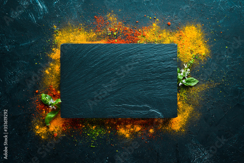 Fototapeta Naklejka Na Ścianę i Meble -  Colorful herbs and spices for cooking. Indian spices. On a black stone background. Top view.