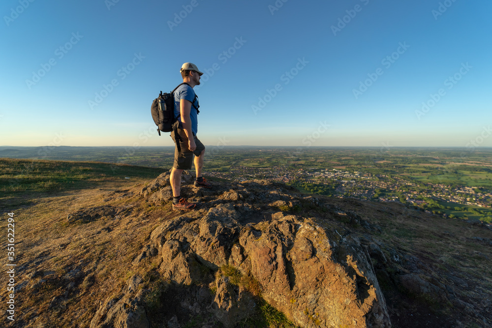 A man standing on a mountain summit overlooking British countryside