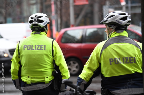 Unrecognizable back turned German policemen with helmets and yellow reflective jacket riding bikes