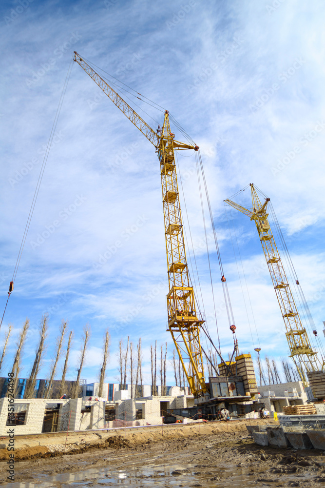 Photos of high-rise construction cranes and an unfinished house against a blue sky. Photographed on a wide angle lens.