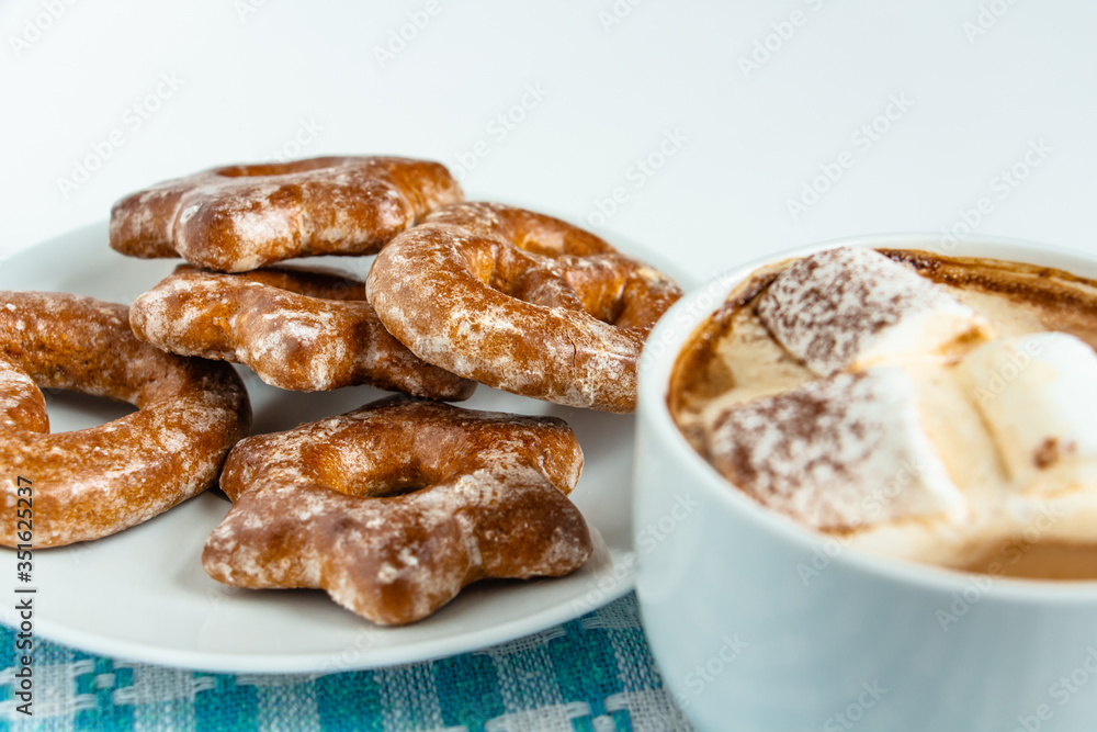 fragrant gingerbread cookies on a white plate with a cup of warm cocoa or coffee with marshmallow, sprinkled with chocolate, white background, blue napkin, delicious dessert, feeling of comfort fragrant gingerbread cookies on a white plate with a cup of warm cocoa or coffee with marshmallow, sprinkled with chocolate, white background, blue napkin, delicious dessert, feeling of comfort