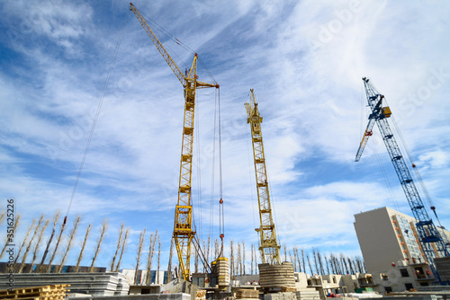 Photos of high-rise construction cranes and an unfinished house against a blue sky. Photographed on a wide angle lens. © sheikoevgeniya