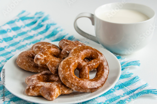 fragrant gingerbread cookies on a white plate with a cup of warm fresh milk, white background, blue napkin, delicious dessert, creating a feeling of homeliness