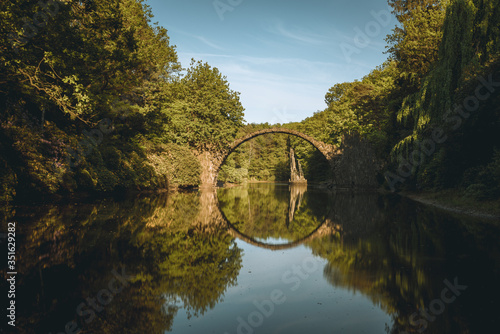 Rakotz bridge Rakotzbrucke also known as Devil's Bridge in Kromlau, Germany. Reflection of the bridge in the water create a full circle. Beautiful summer day with blue sky and clouds.