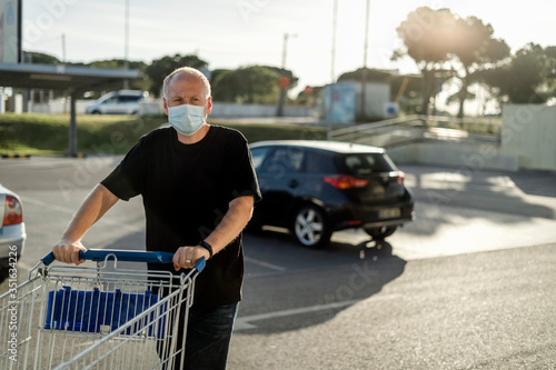 Man wearing protective facial mask pushing shopping cart