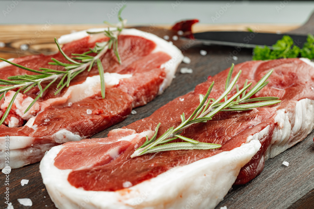 Raw meat steaks with herbs on wooden board