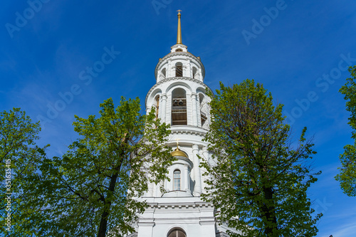 Obraz na płótnie bell tower against a blue sky, in the foreground trees w salonie