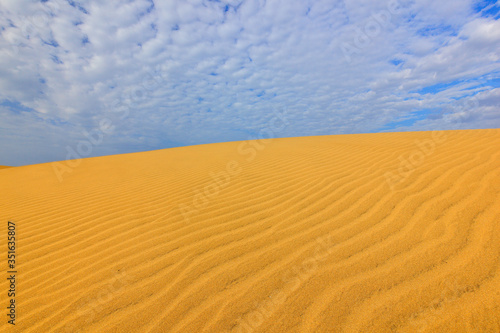 Summer dry landscape in Africa. Black pebble stones. Sandy waves in the wild nature. Dunas Maspalomas  Gran Canaria  Spain. Beautiful rare blue sky with white clouds.