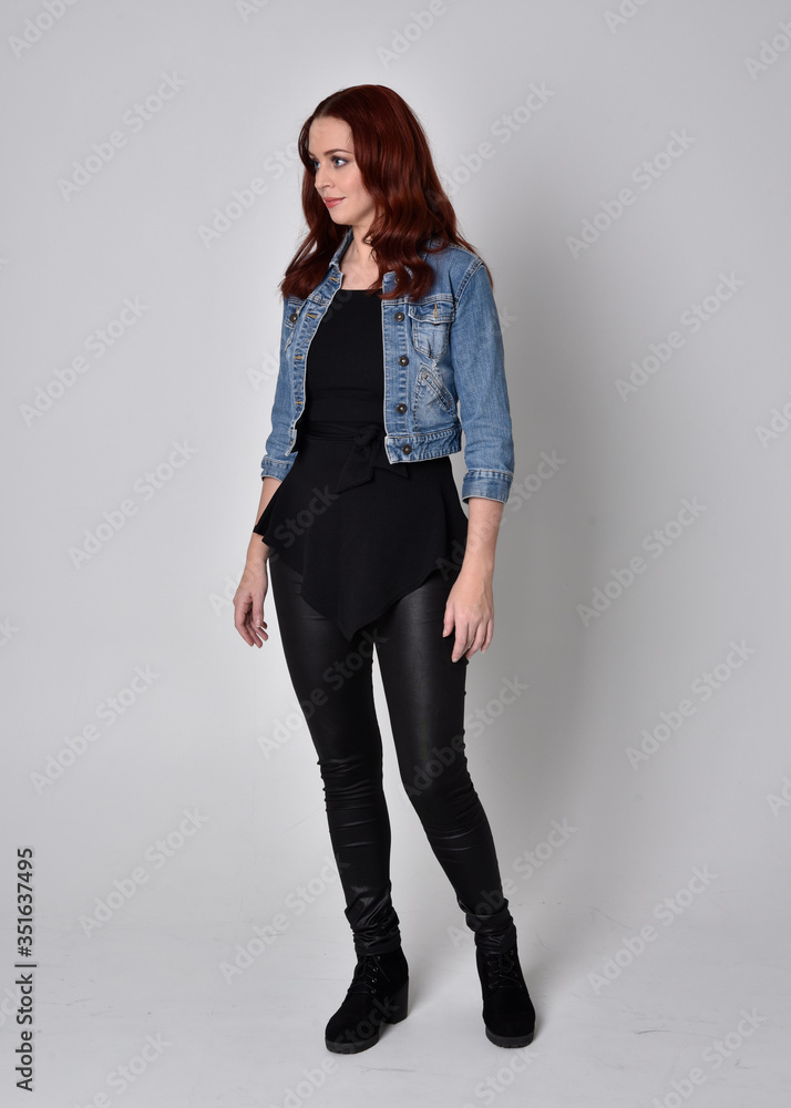 portrait of a pretty girl with red hair wearing black leather pants and top. Full length standing pose isolated against a grey studio background portrait of a pretty girl with red hair wearing black leather pants and top. Full length standing pose isolated against a grey studio background