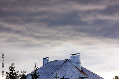 the sky is covered with storm clouds on the background of the roof of the house © albert