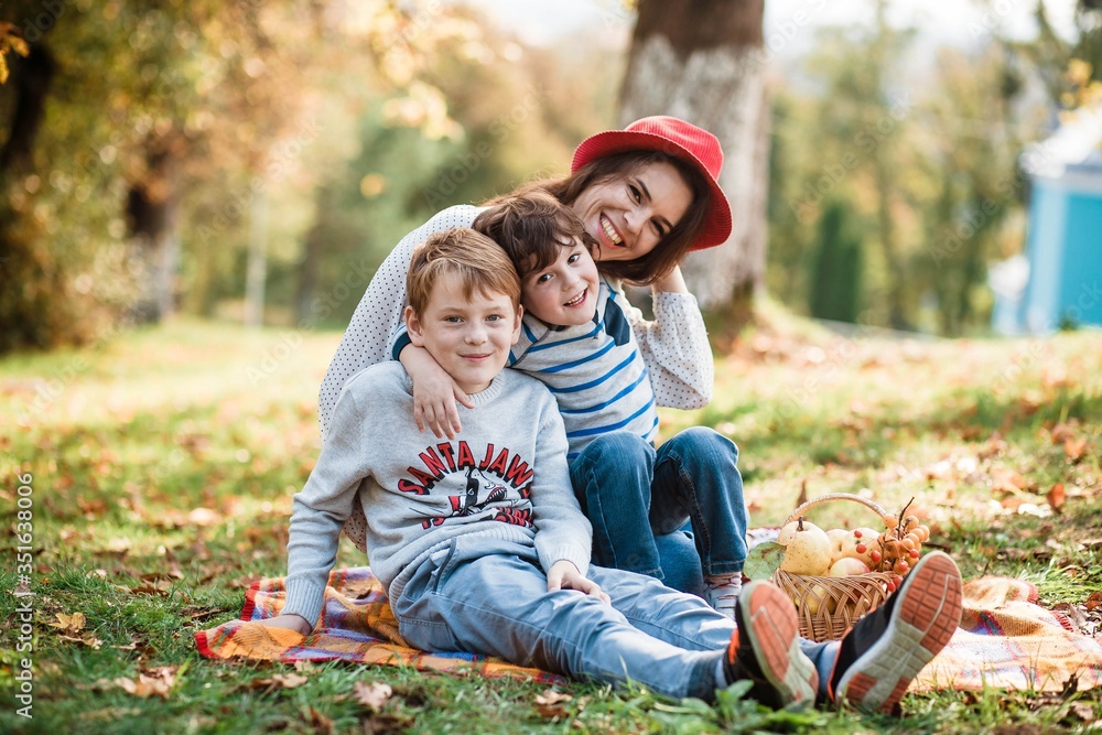 Fototapeta premium Such love, which is impossible to describe, only to feel. Mothers and sons. Happy Mother's Day! Mother hugs her children on a background of forest. Family. Mom and children are sitting on the mat.