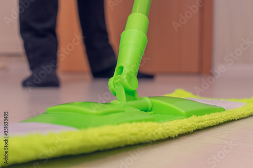 Mop in the foreground  guyl washes the floor in his house  men s legs  close up  toned  cropped image