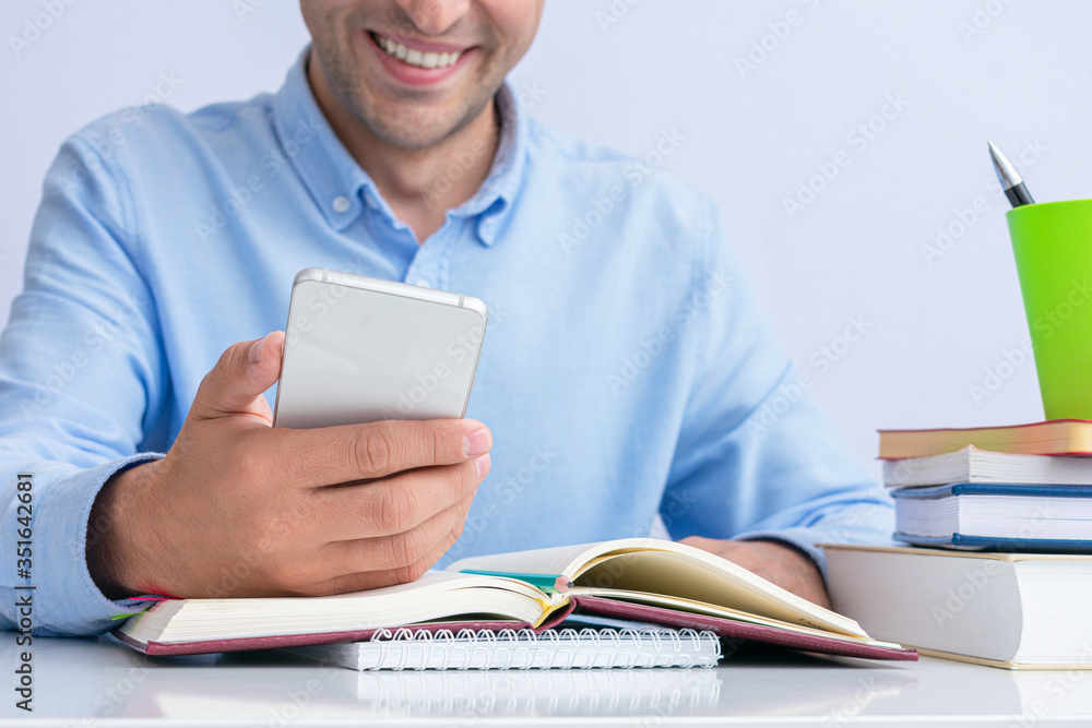 Smiling student preparing for exams and uses phone, men's hands, cropped image, close up Smiling student preparing for exams and uses phone, men's hands, cropped image, close up