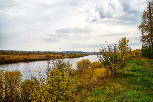 View on the river from top place on the bank through branch of trees and sky with clouds background. Nature landscape in an autumn day