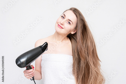 Attractive girl uses a hair dryer, portrait, white background. Hair care, copy space,