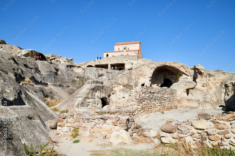 Uplistsikhe, Georgia - October 22, 2020: Tourists in a mountain reserve near ancient old city with rocks, residential and religious caves and blue sky on a Sunny summer day. Uplistsikhe city, Georgia